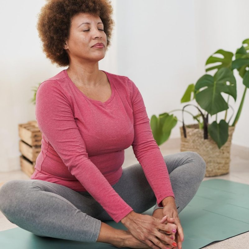 HEALTH_mature-multiracial-woman-doing-yoga-stretching-exercises-home-self-love-healthy-work-life-balance